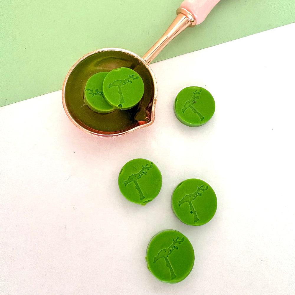Bright green sealing wax beads in pink melting spoon, for botanical themed crafts.
