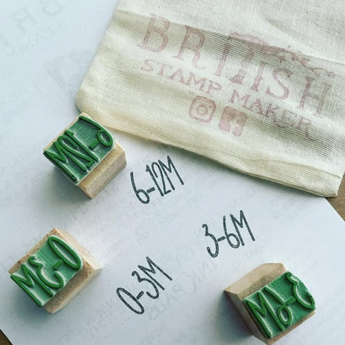 Three wooden stamps with green ink on a white surface, next to a bag labeled 'British Stamp Maker'.