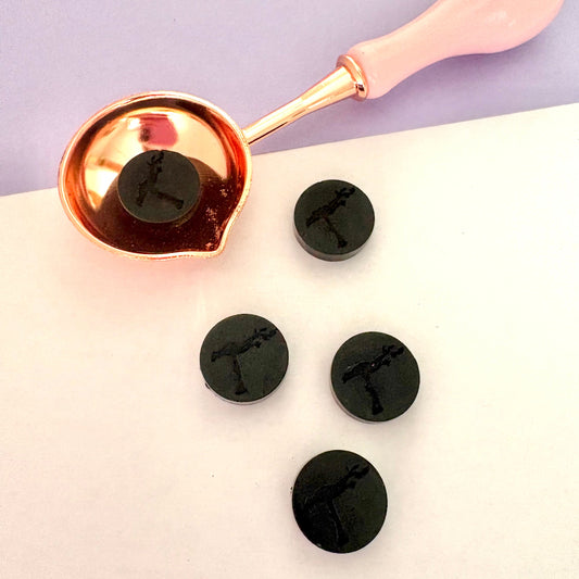 Black sealing wax beads arranged with a pink melting spoon, for dramatic crafting.