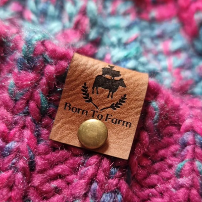 Born to farm logo on brown Vegan Faux leather label attached to a hand knitted hat with a gold rivet fastener.