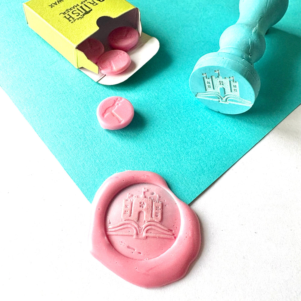Custom Castle and Book wax seal stamp with pink wax melts and impression."