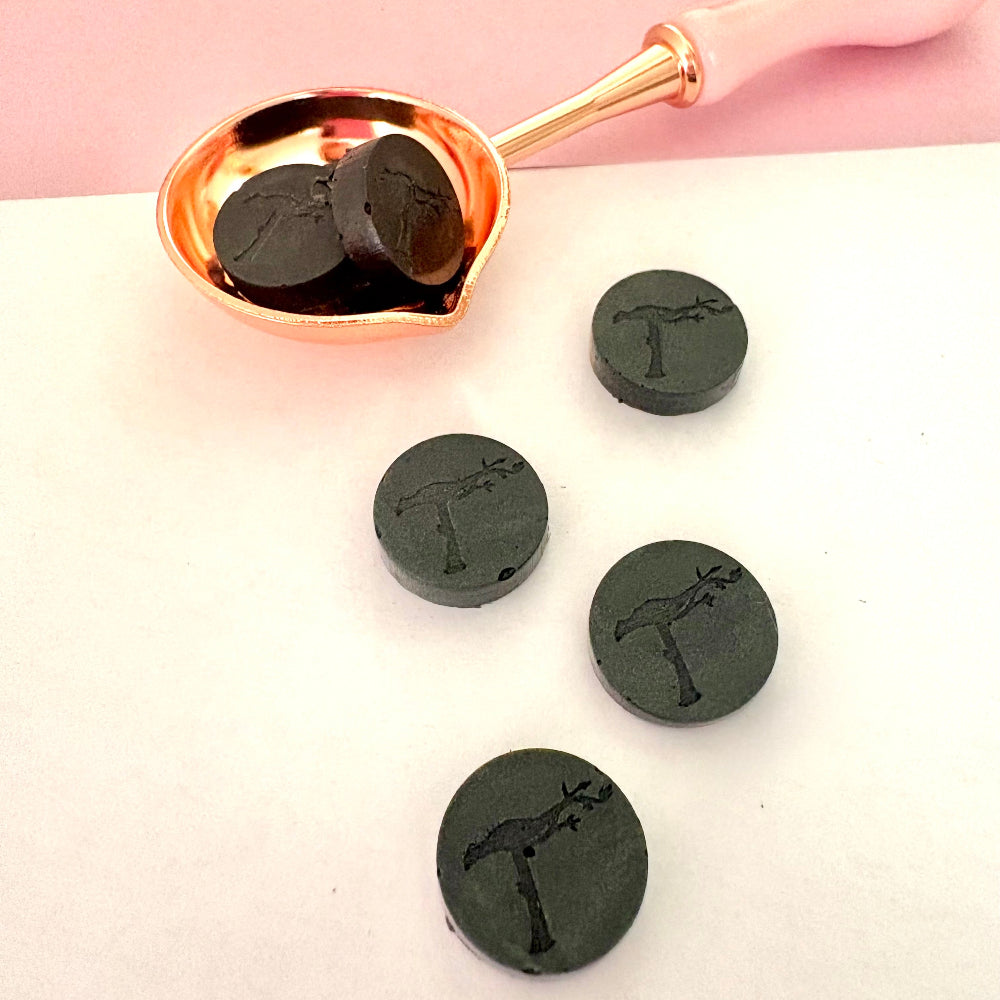 Elegant grey sealing wax beads in melting spoon, showing subtle texture.