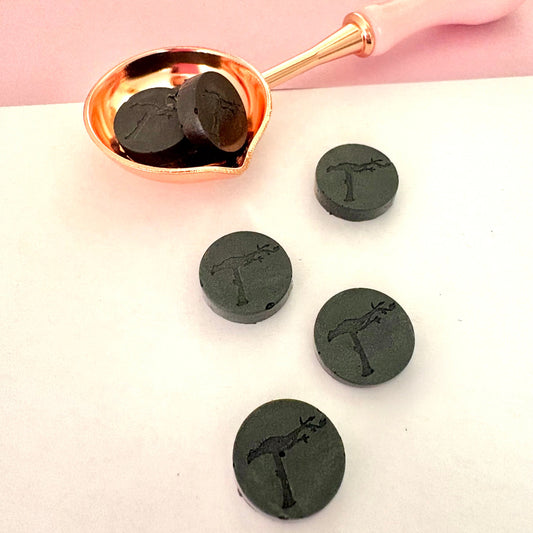 Elegant grey sealing wax beads in melting spoon, showing subtle texture.