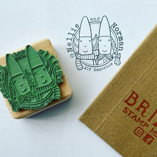 Nellie and Norman Elf Emporium rubber stamp printed on white paper. The stamp is vegan eco green rubber with a reclaimed wooden block and the corner of a lil packaging box is featured in this image.