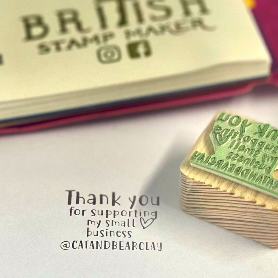 Thank you for supporting my small business eco rubber stamp, stamped in black ink on white paper. Pink notebook in the background with British stamp maker printed. Traditional style reclaimed wood stamp block with green vegan eco rubber.
