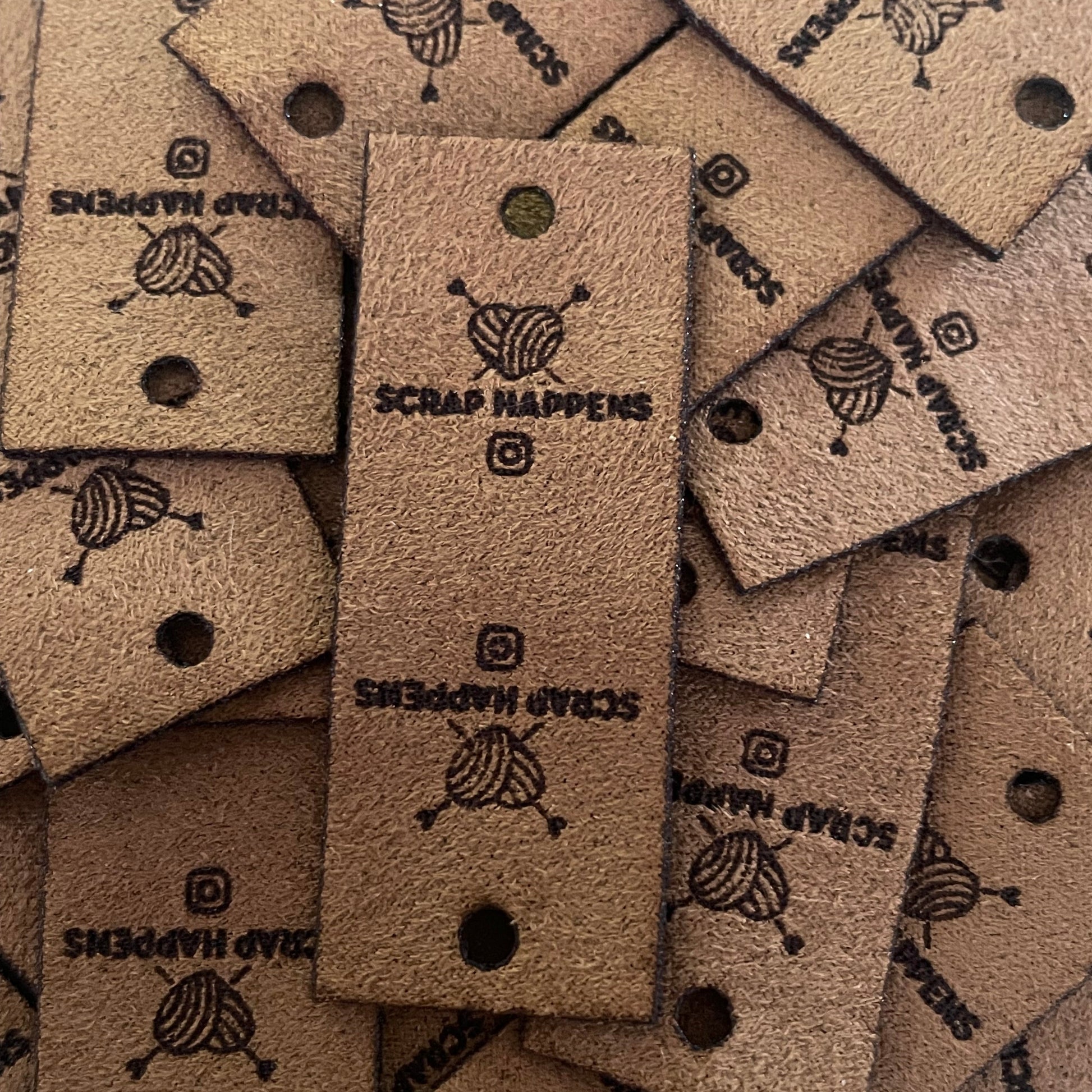 Brown faux suede tag with square edges, one hole for a rivet attachment. Featuring scrap happens logo and a instagram icon.