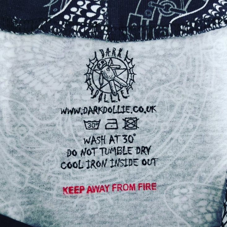 Garment care stamp including dark dollie logo, wash symbols, wash at 30 text, do not tumble dry, cool iron inside out and www.darkdollie.co.uk website address in black ink. KEEP AWAY FROM FIRE in red ink on the inside of handmade clothing.